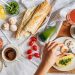 Overhead shot of a delicious breakfast flatlay featuring fresh ingredients and coffee on a white tablecloth.